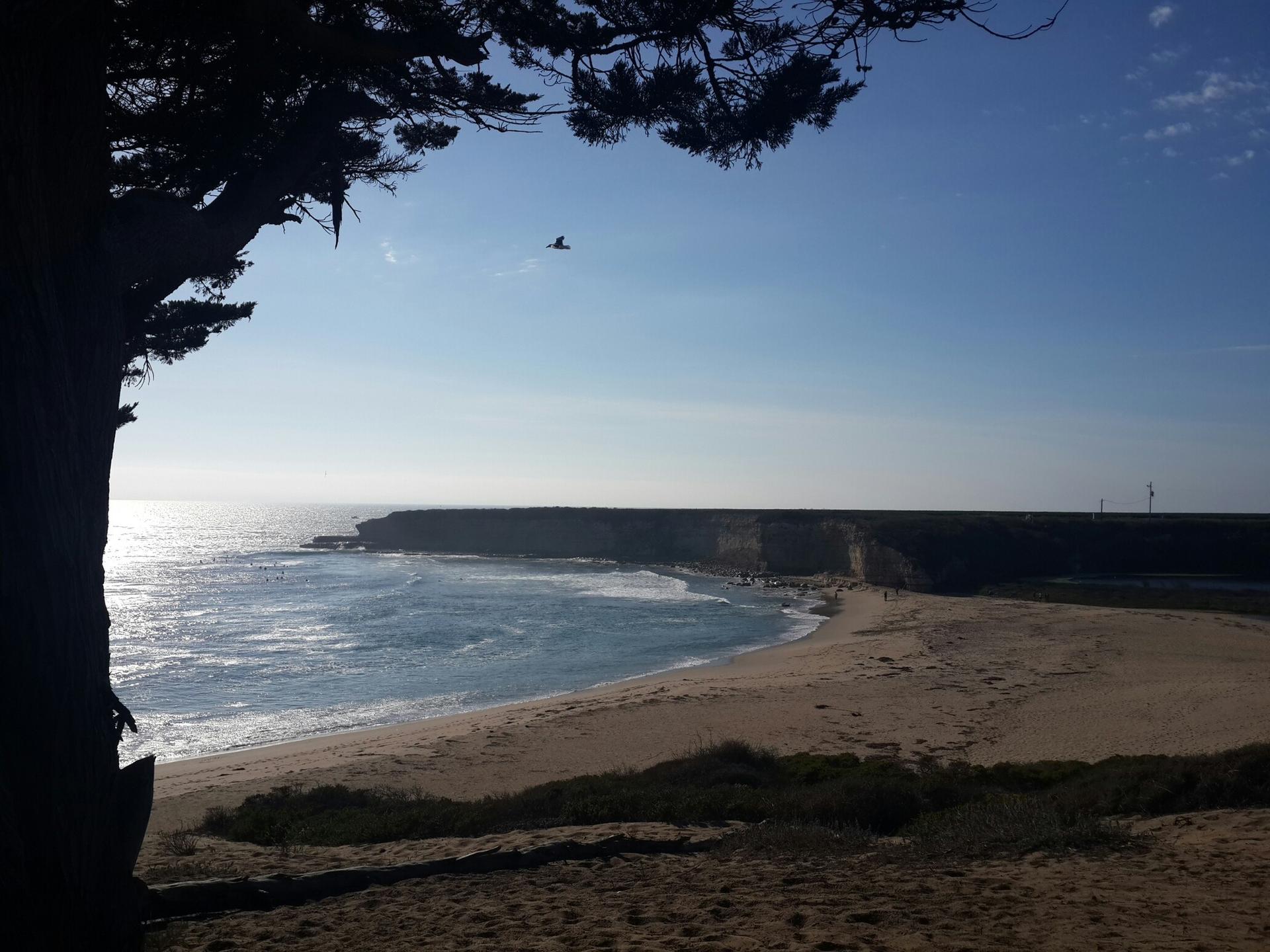 Sunny coastal view with a wide sandy beach, ocean, and distant cliffs.