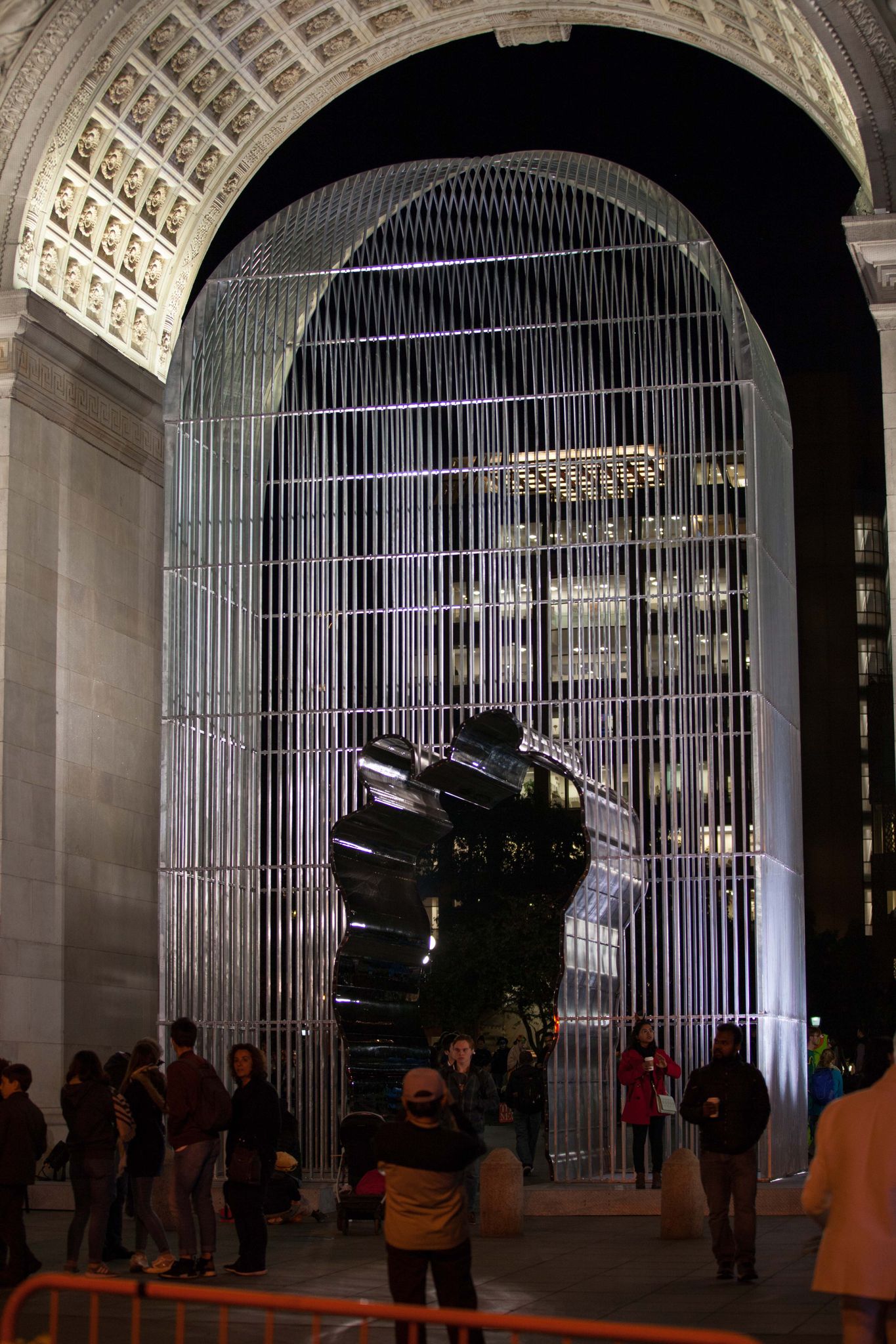 Nighttime view of a large metal cage art installation under an arch, with people. - Chinatown & Little Italy via Washington Square Park loop