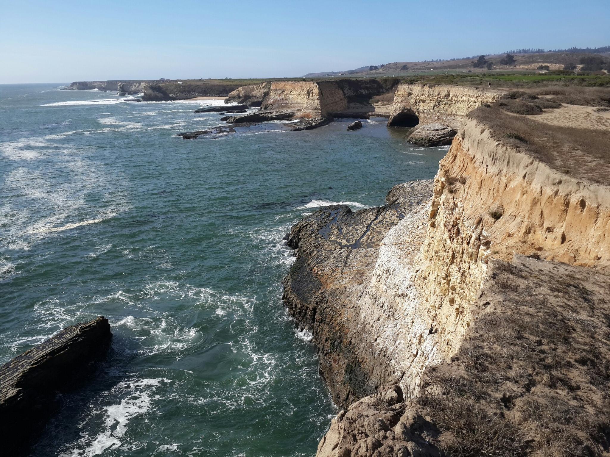 Rugged sea cliffs and turbulent ocean waves under a bright sky.