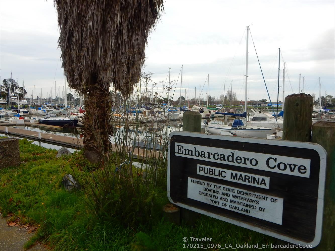 A marina sign in front of docked sailboats under a cloudy sky.