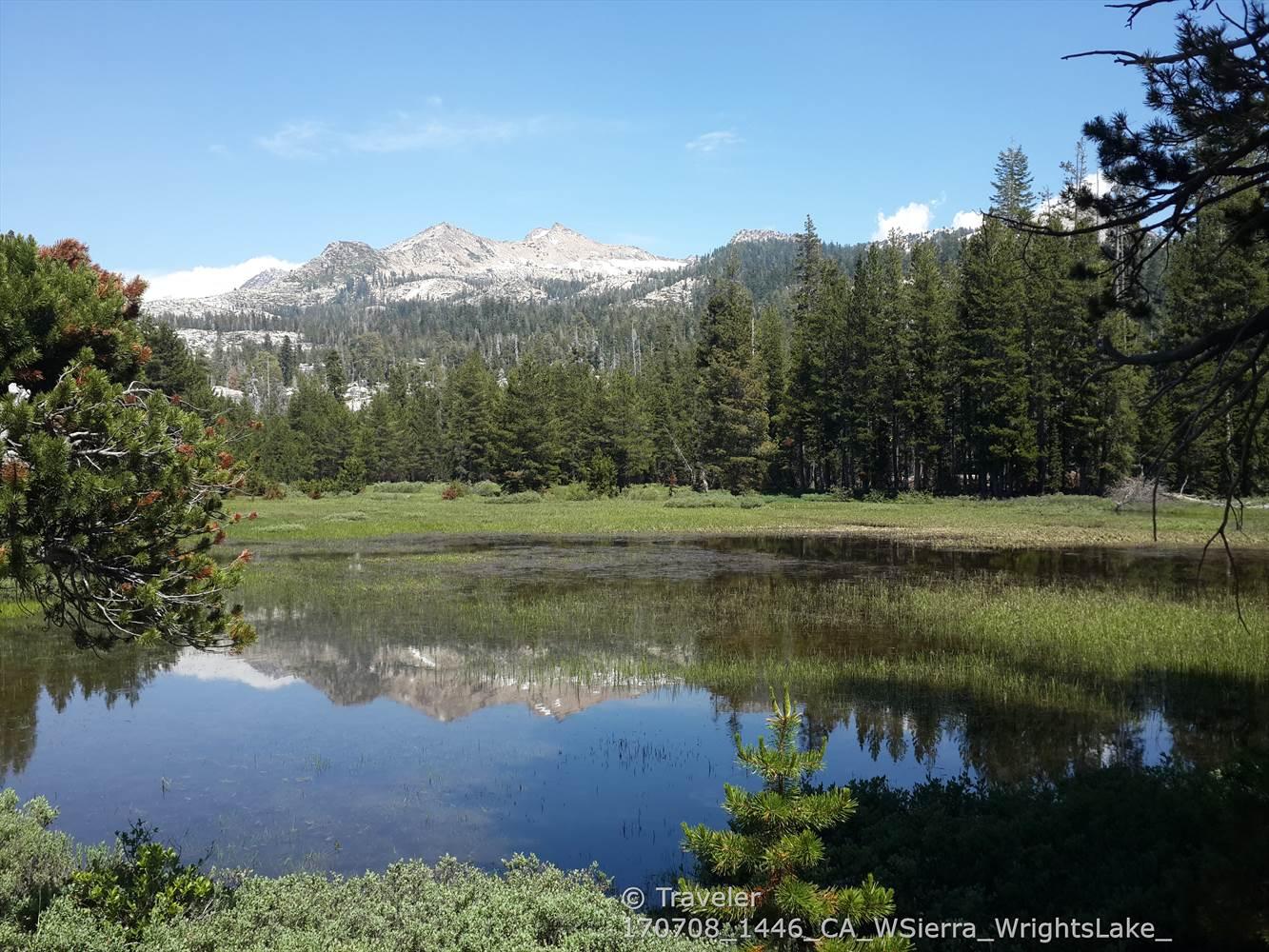 A serene lake reflecting snow-capped mountains and green forests on a clear day.