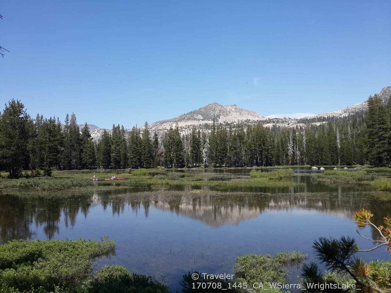 Serene lake reflecting distant mountains and forest under a clear sky.