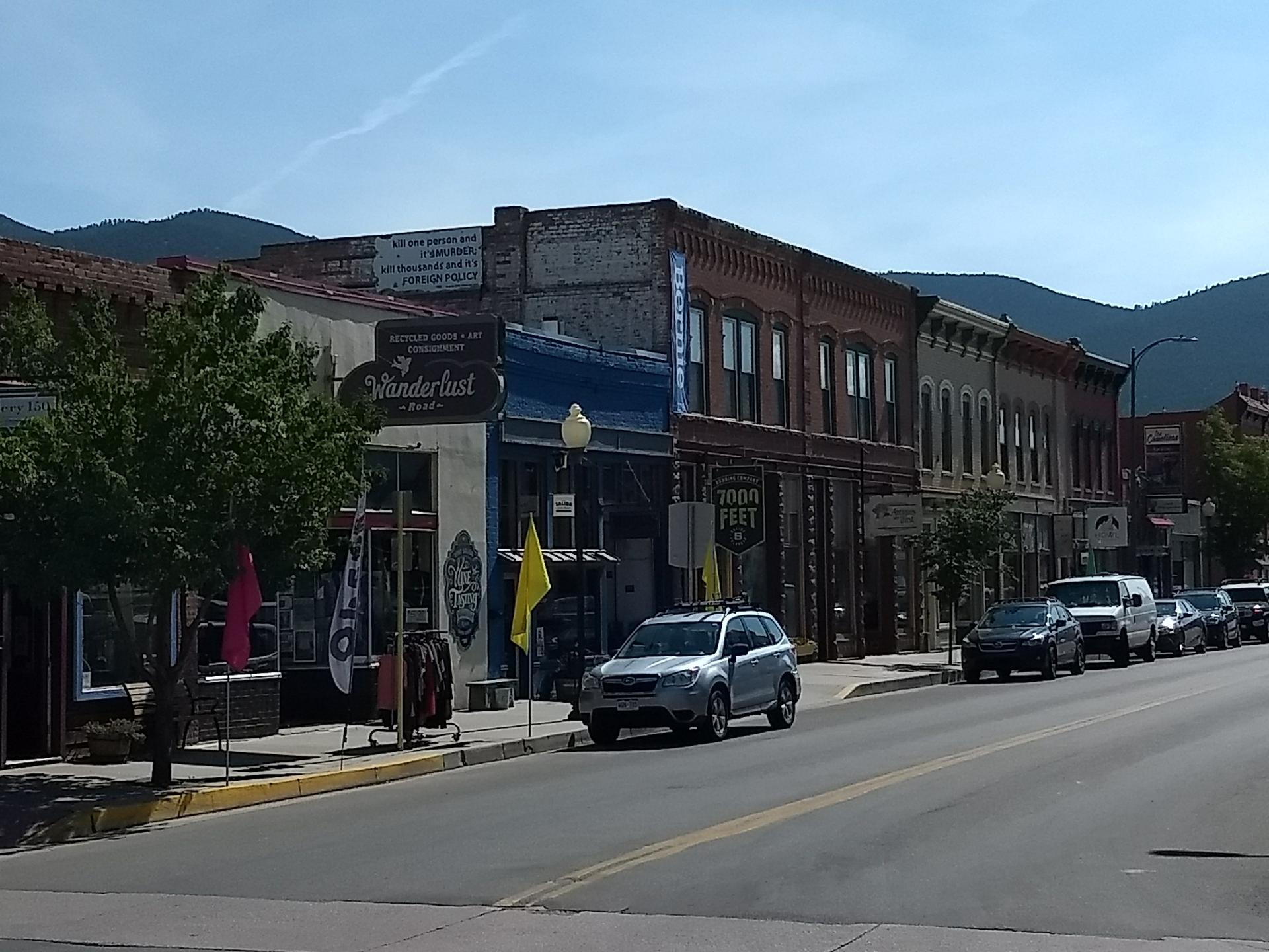 Bright daylight illuminates a street lined with historic brick buildings and parked cars.