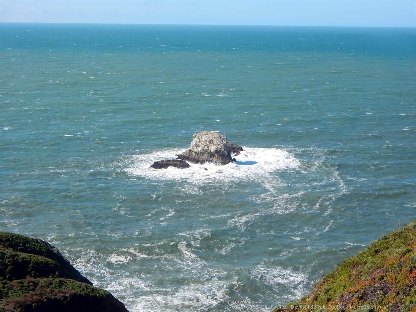 Large sea stack in choppy ocean water with white foam.