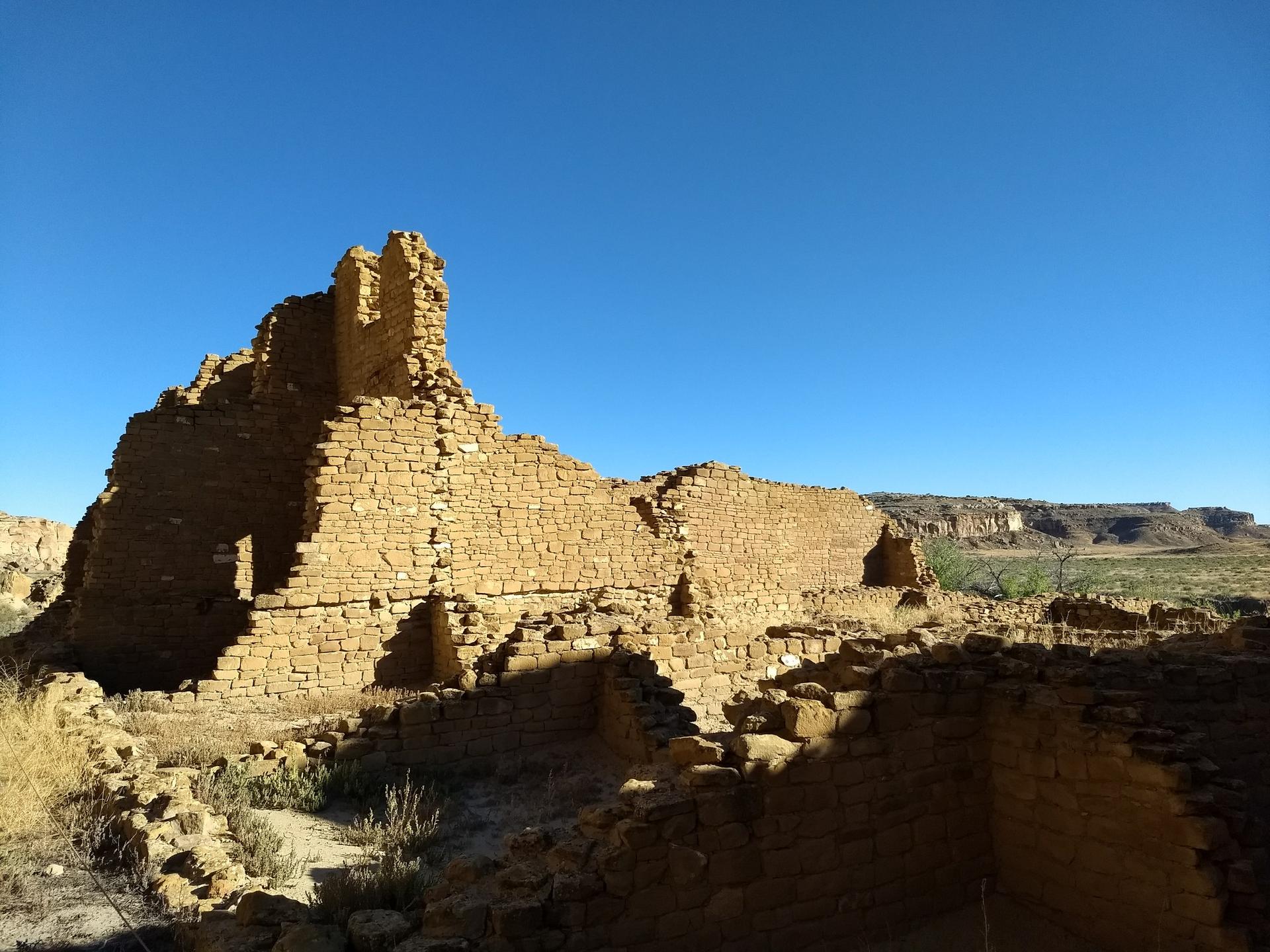 Ancient stone ruins under a clear blue sky, casting long shadows.