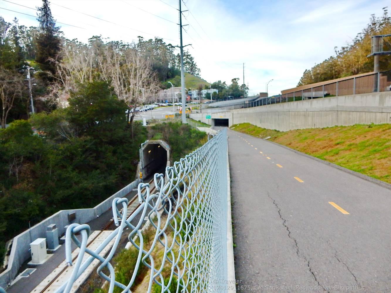 Paved road next to a chain-link fence and a train tunnel.