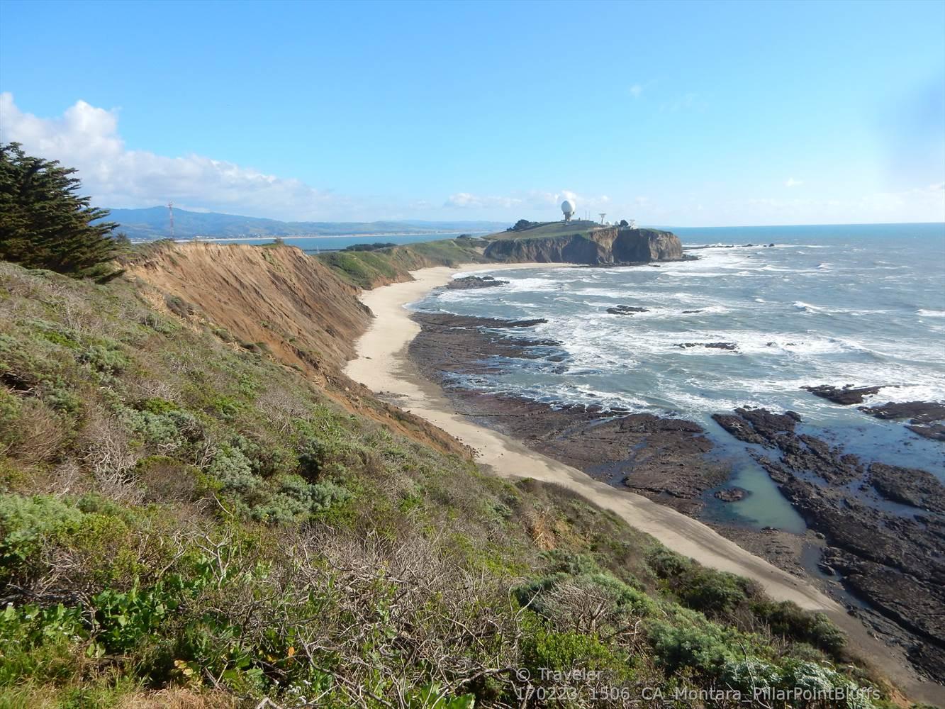Coastal view with a sandy beach, rocky shore, and distant headland.