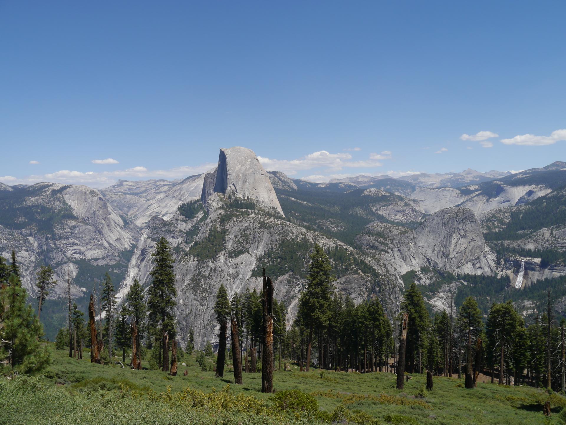 A prominent granite dome rises above a vast, forested mountain landscape.