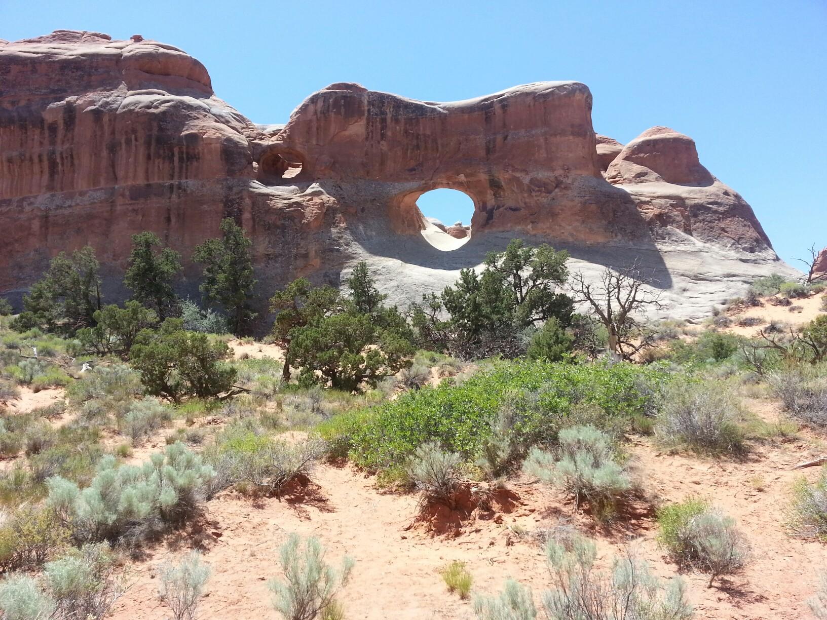 A natural rock arch in a large red rock formation above desert shrubs.