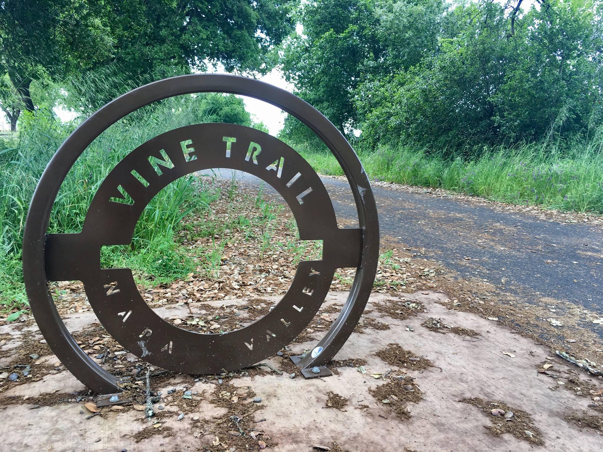 A metal circular sign for a trail next to a paved path.
