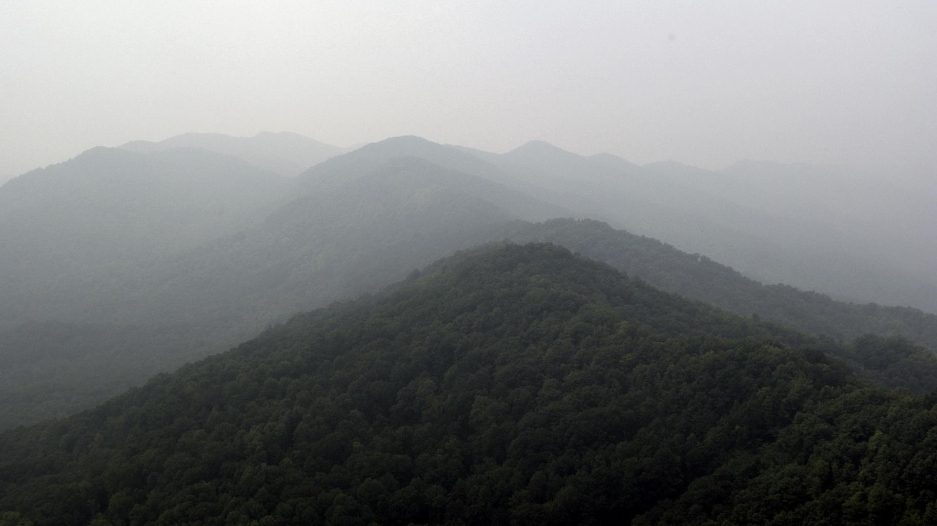 Hazy view of multiple layers of forested mountains under an overcast sky.