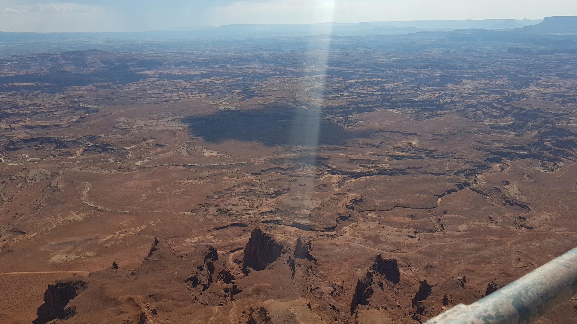 Aerial view of a vast, sunlit desert landscape with canyons and mesas.