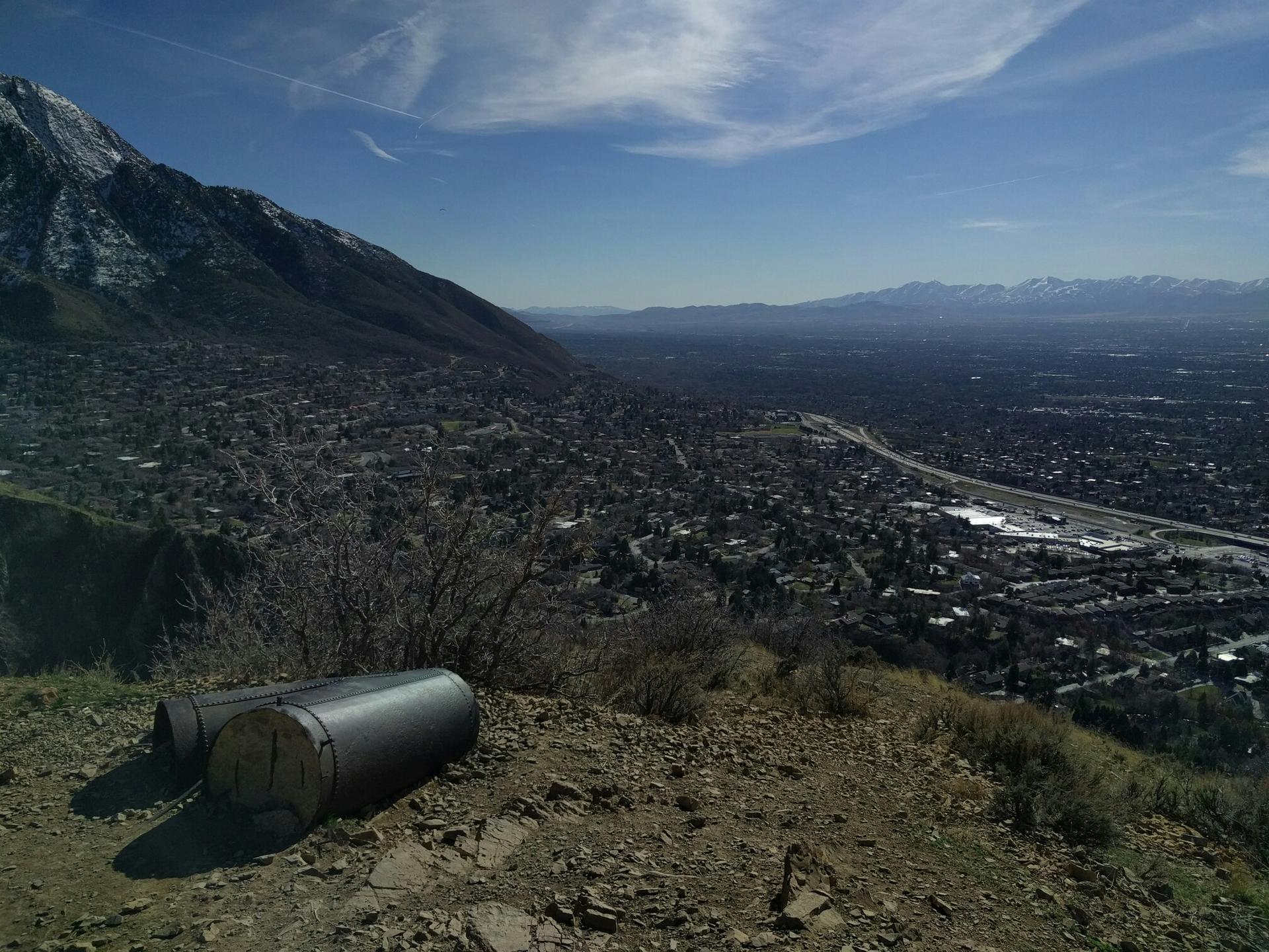Cylindrical objects on a hill overlooking a town and mountains under a clear sky.