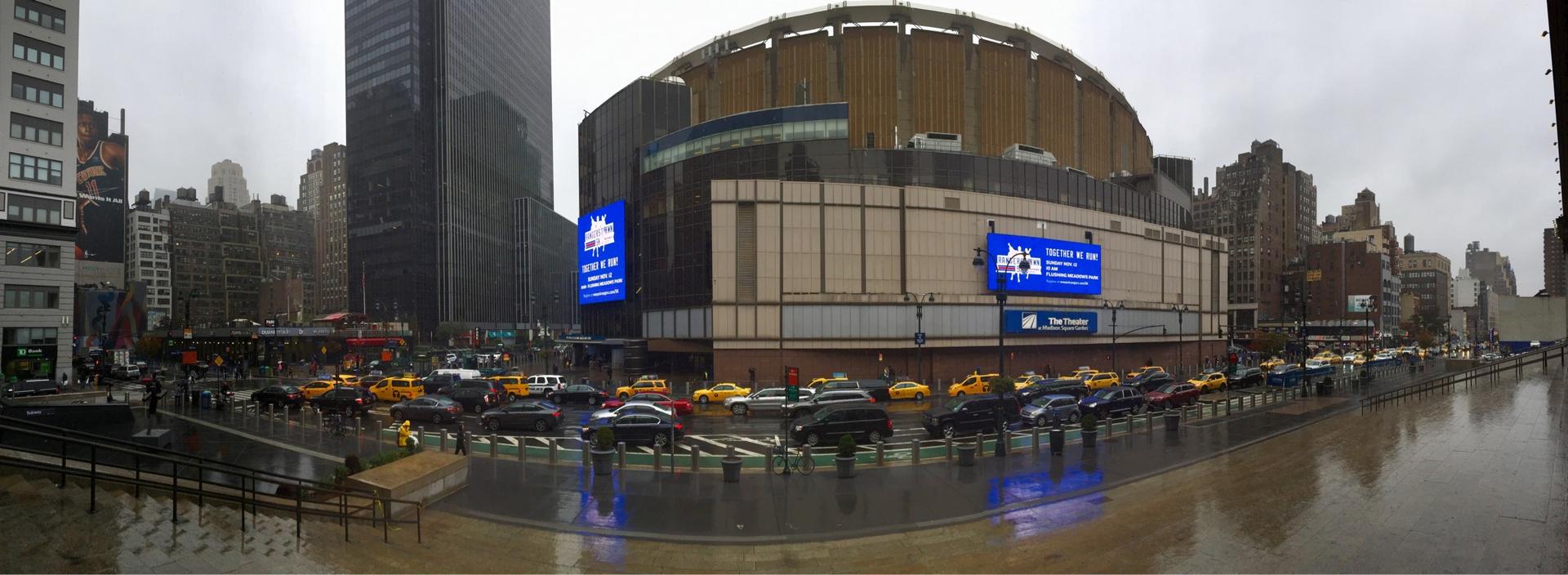 Large round building with blue signs, taxis line a wet city street.