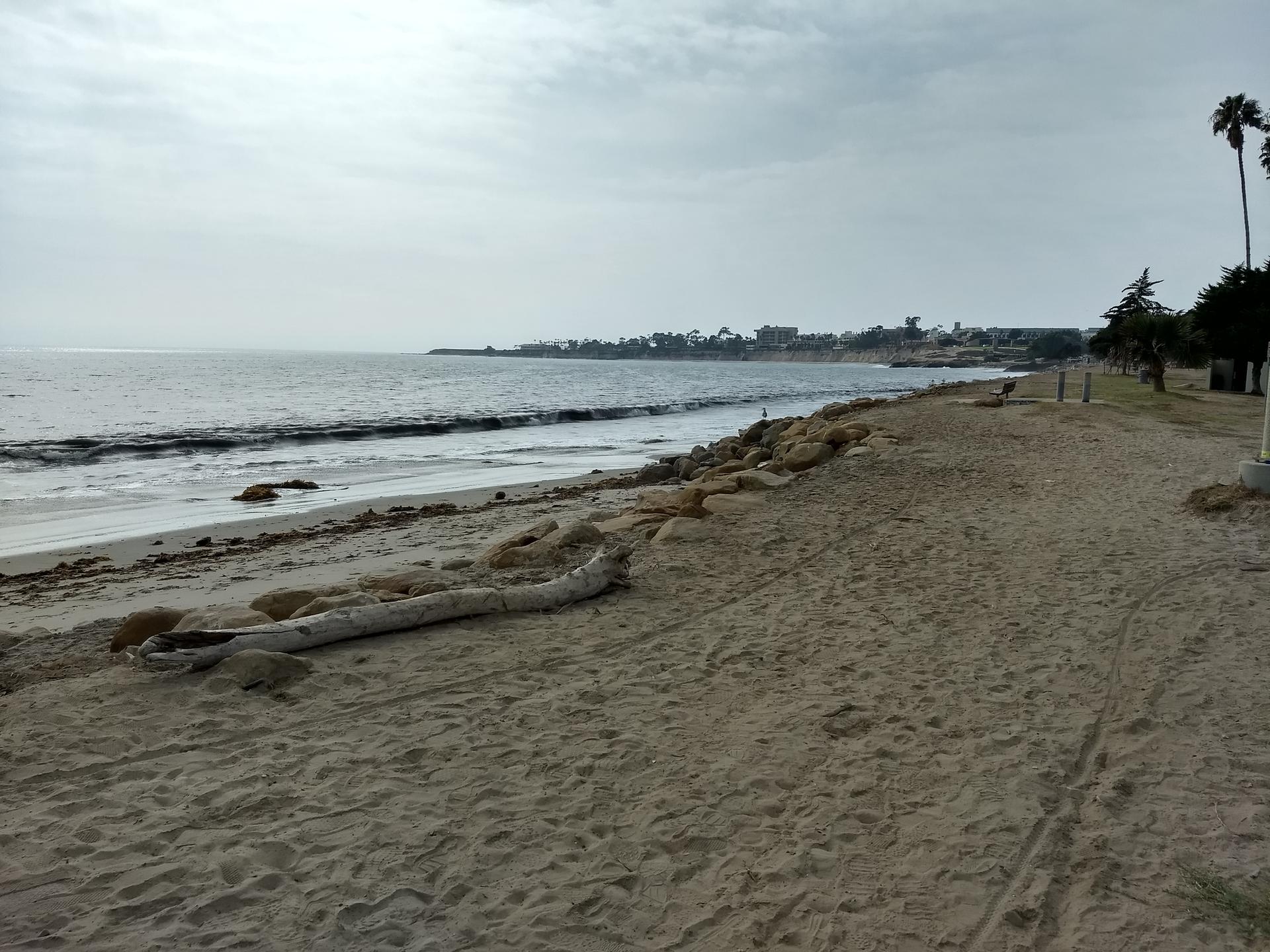A wide sandy beach with gentle ocean waves under an overcast sky.