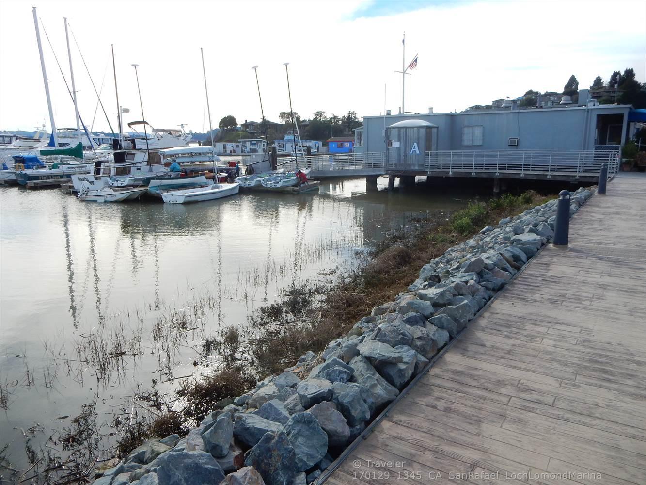 Boats docked in a marina next to a building and wooden walkway.