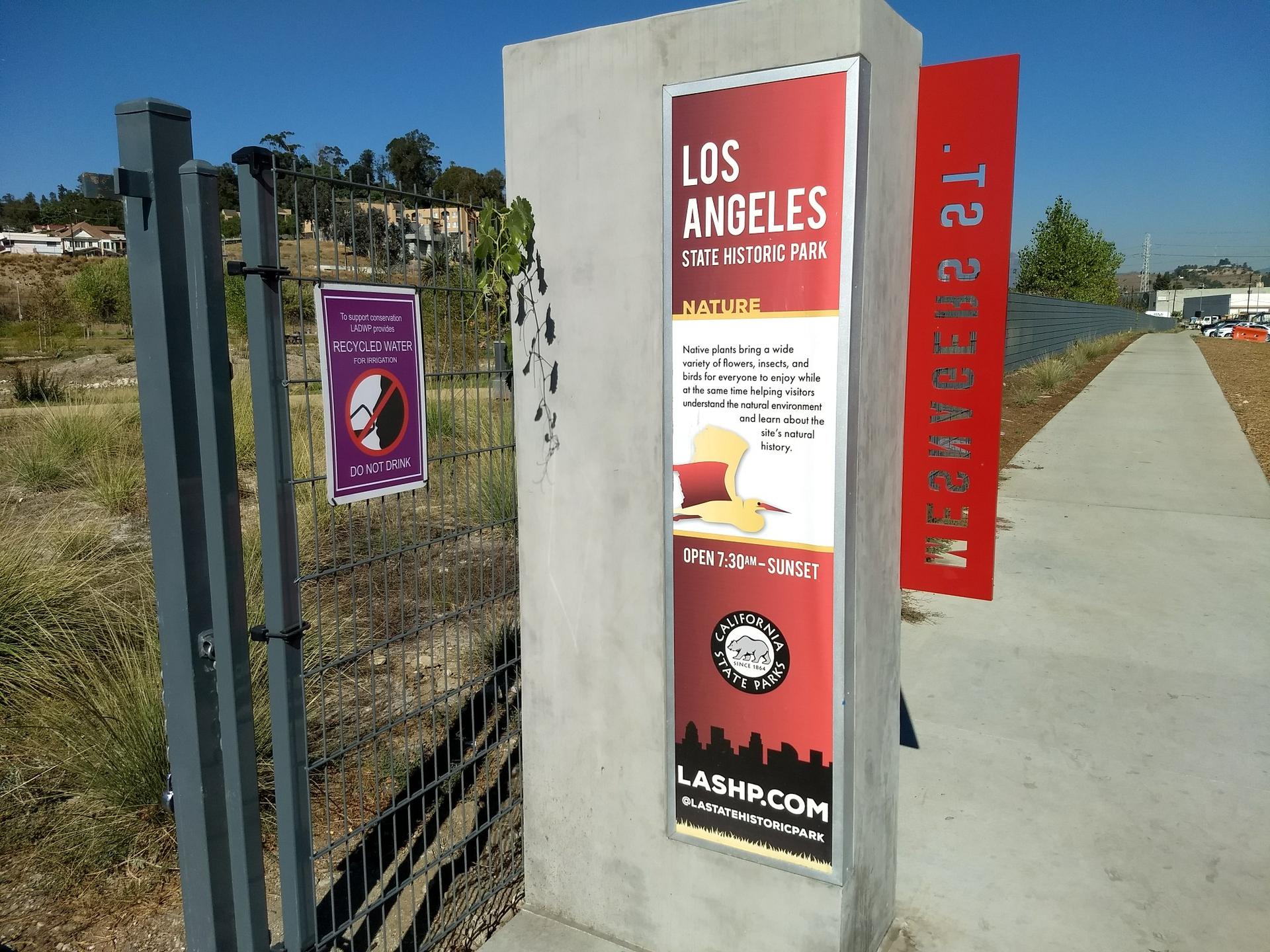 An information sign on a concrete pillar next to a fence on a sunny day.