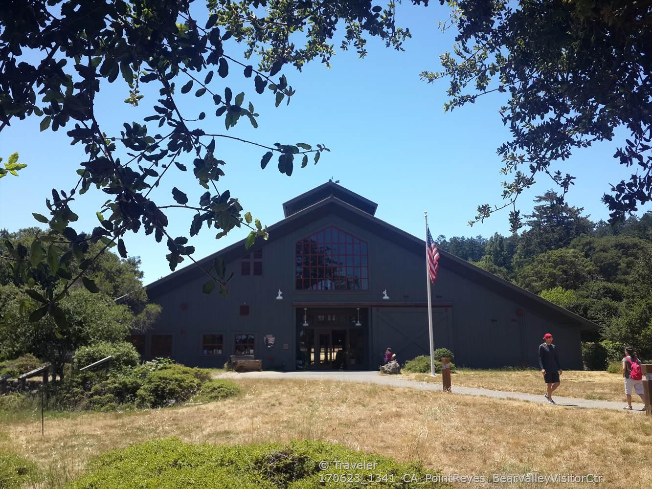 Large barn-like building with an American flag, people walking on a sunny day.