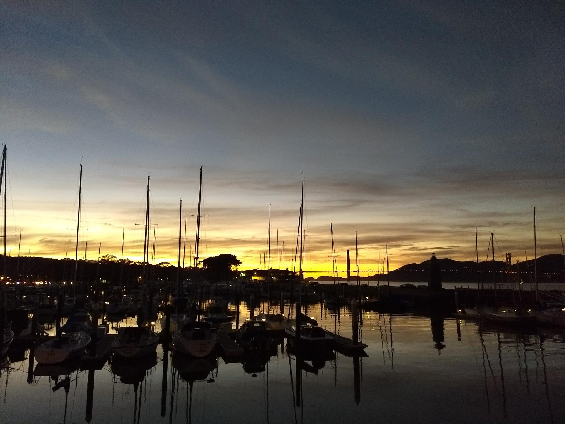 Silhouetted sailboats in a marina at sunset with vibrant orange and blue sky.