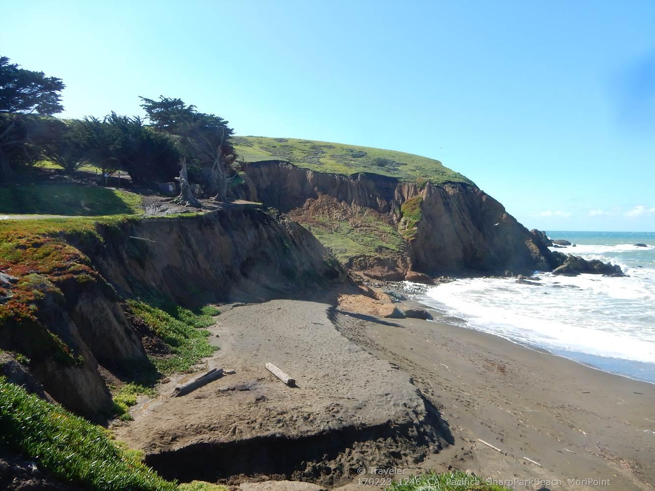 Sunny view of rugged coastal cliffs, a small beach, and ocean waves.