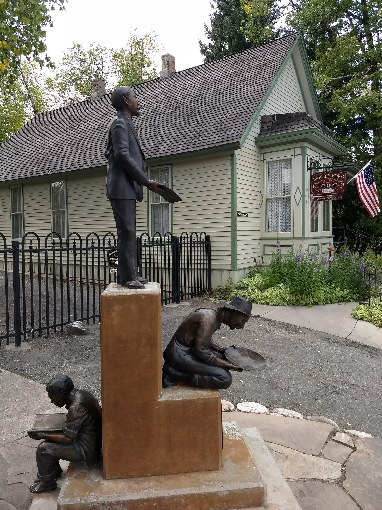 Bronze statues of prospectors in front of an old building with an American flag.