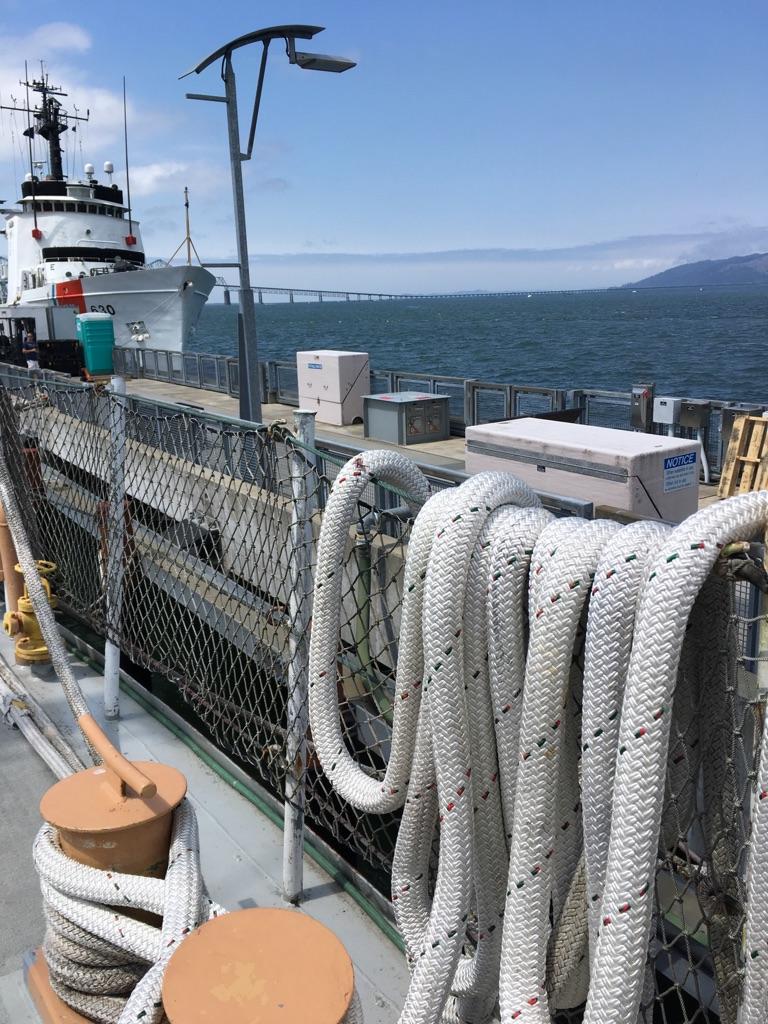 Large white ship docked, coiled ropes in foreground, bright sunny day.