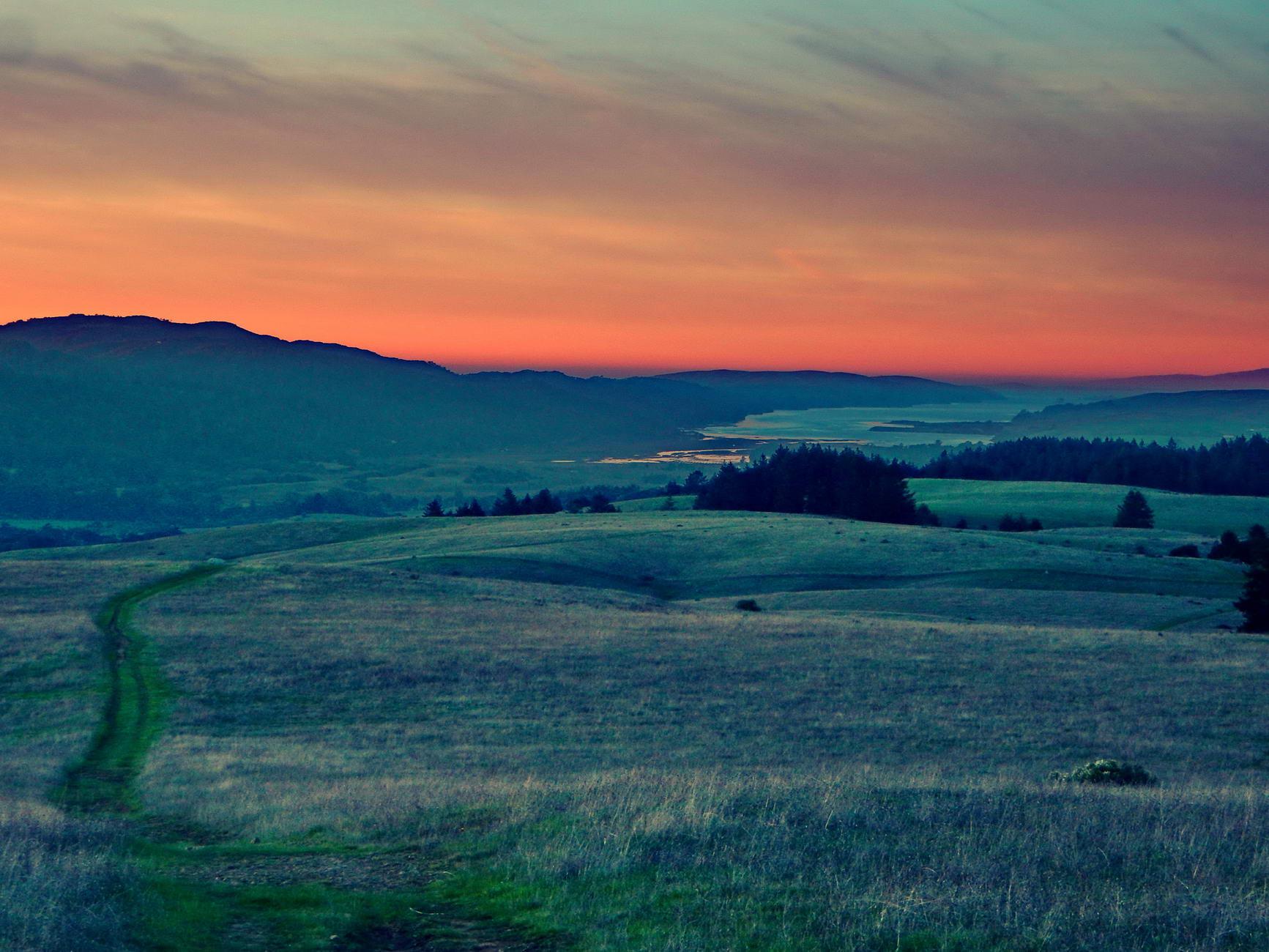 Rolling grassy hills under a vibrant orange and blue sunset sky.