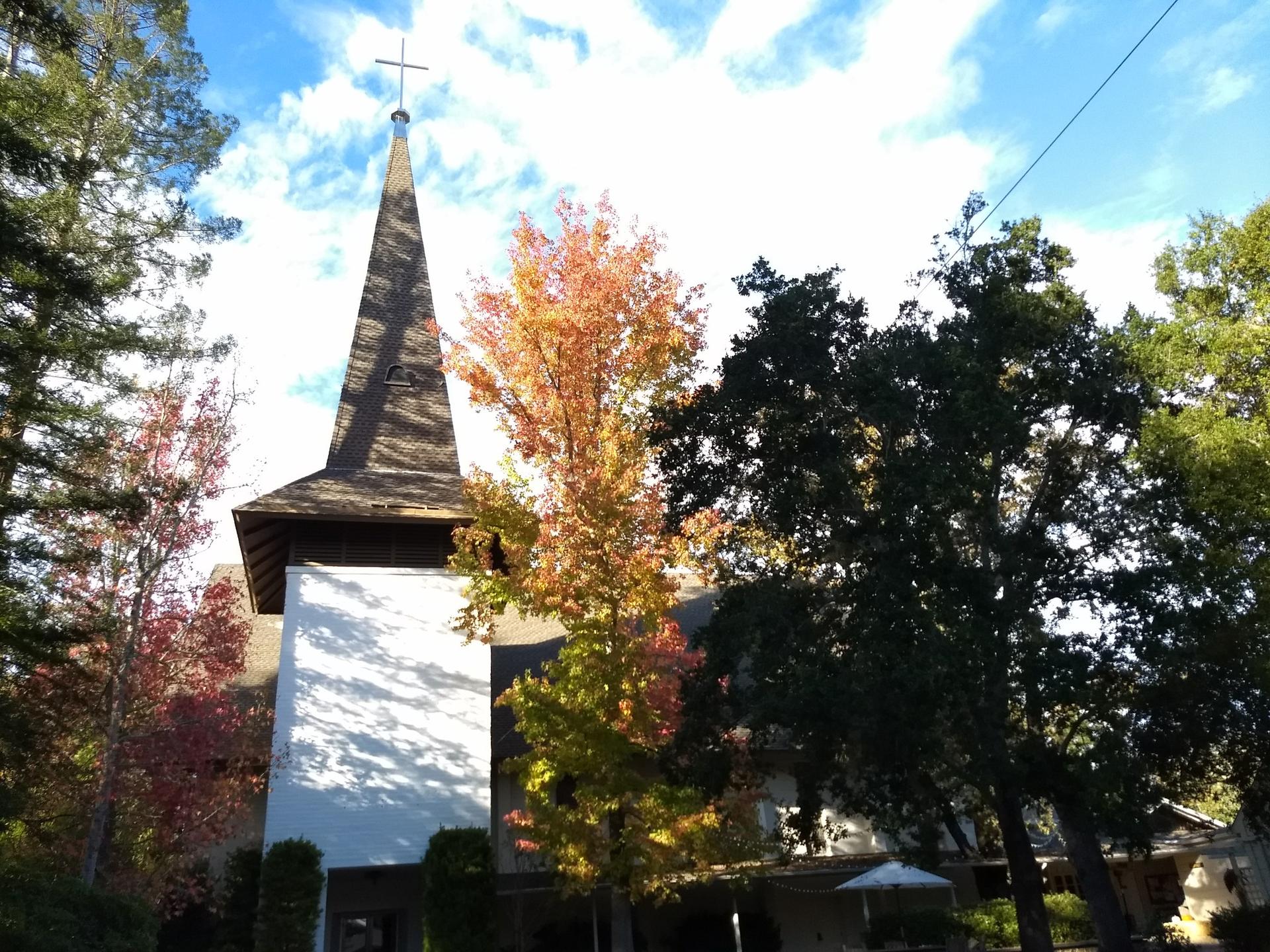 Church steeple with a cross, surrounded by colorful autumn trees.