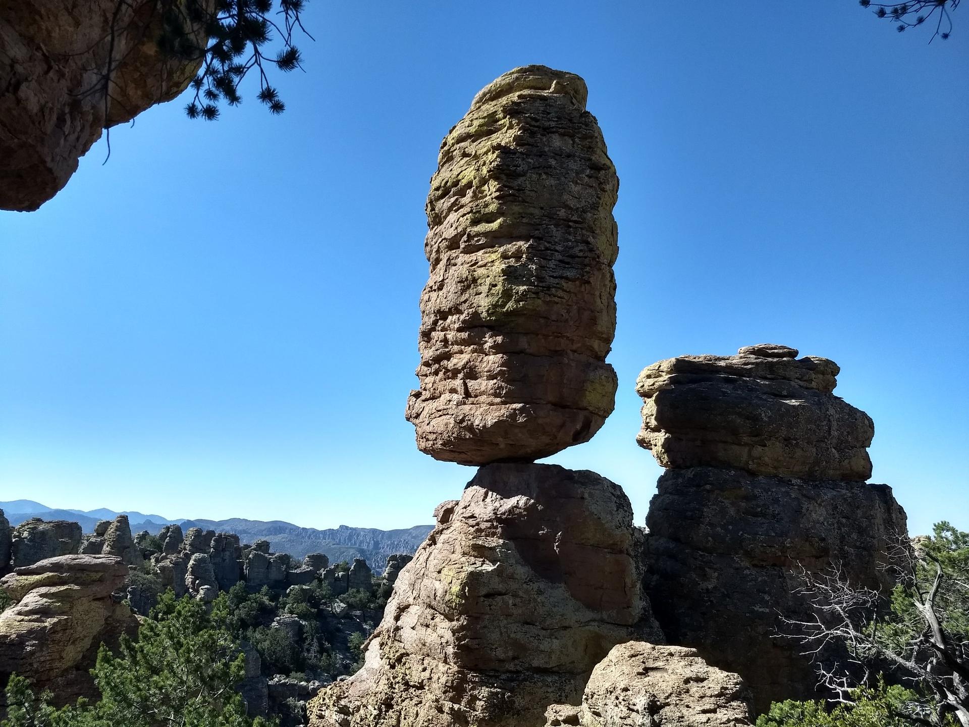 A tall, balanced rock formation against a bright blue sky.