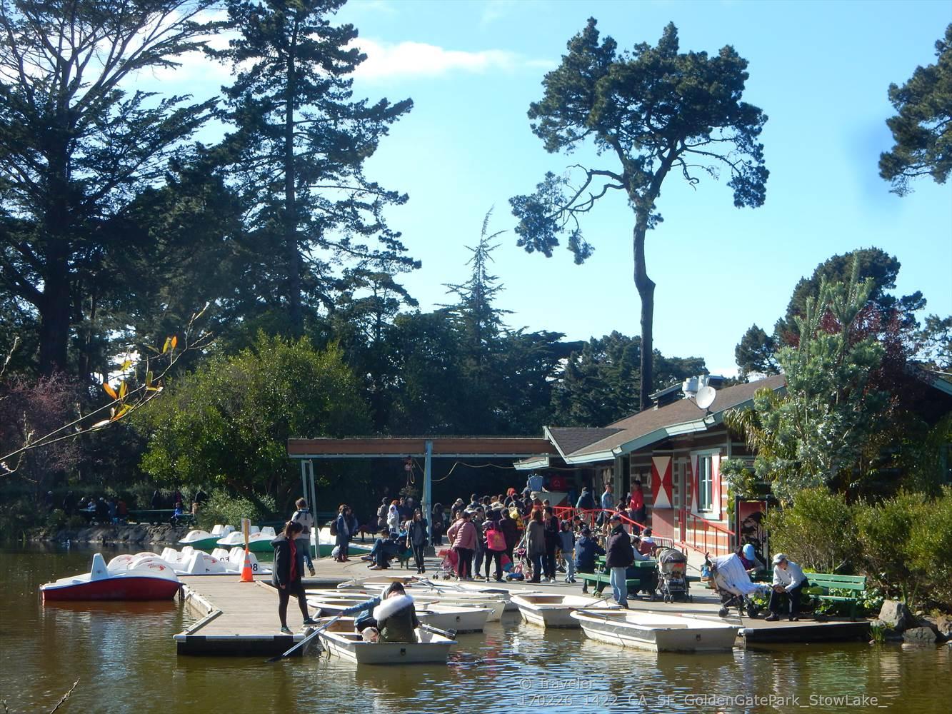People gathered at a boathouse and docks with paddle boats on a lake.
