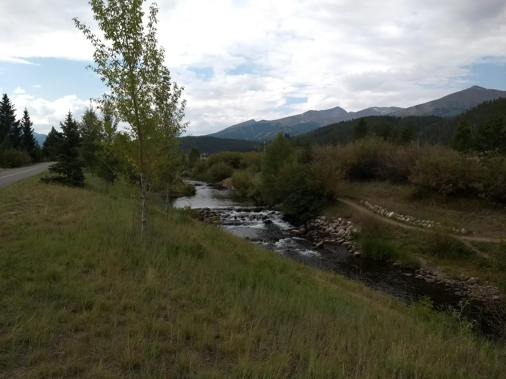 A winding river in a mountain landscape with green trees and cloudy sky.