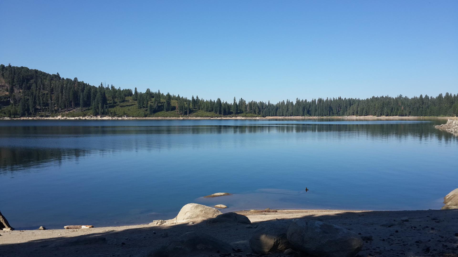 Serene lake with forested hills under a clear blue sky.