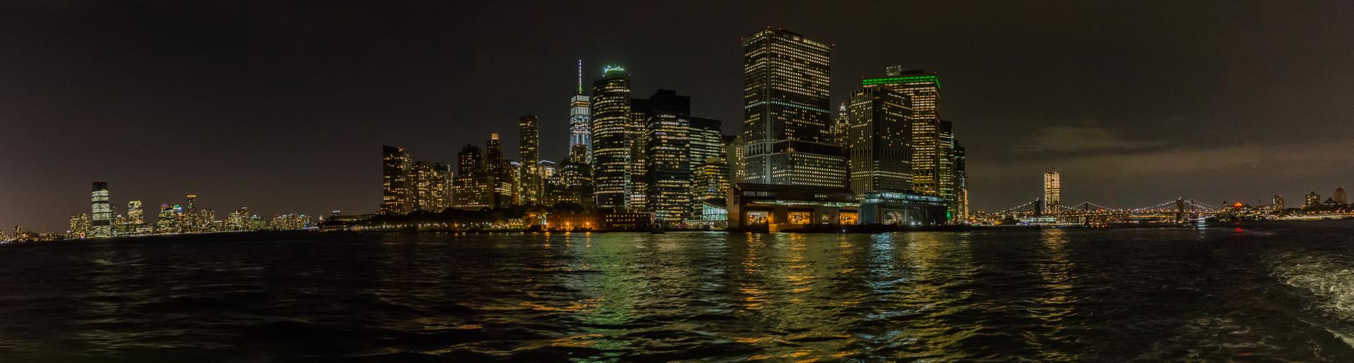 Night panorama of a brightly lit city skyline reflecting on dark water.