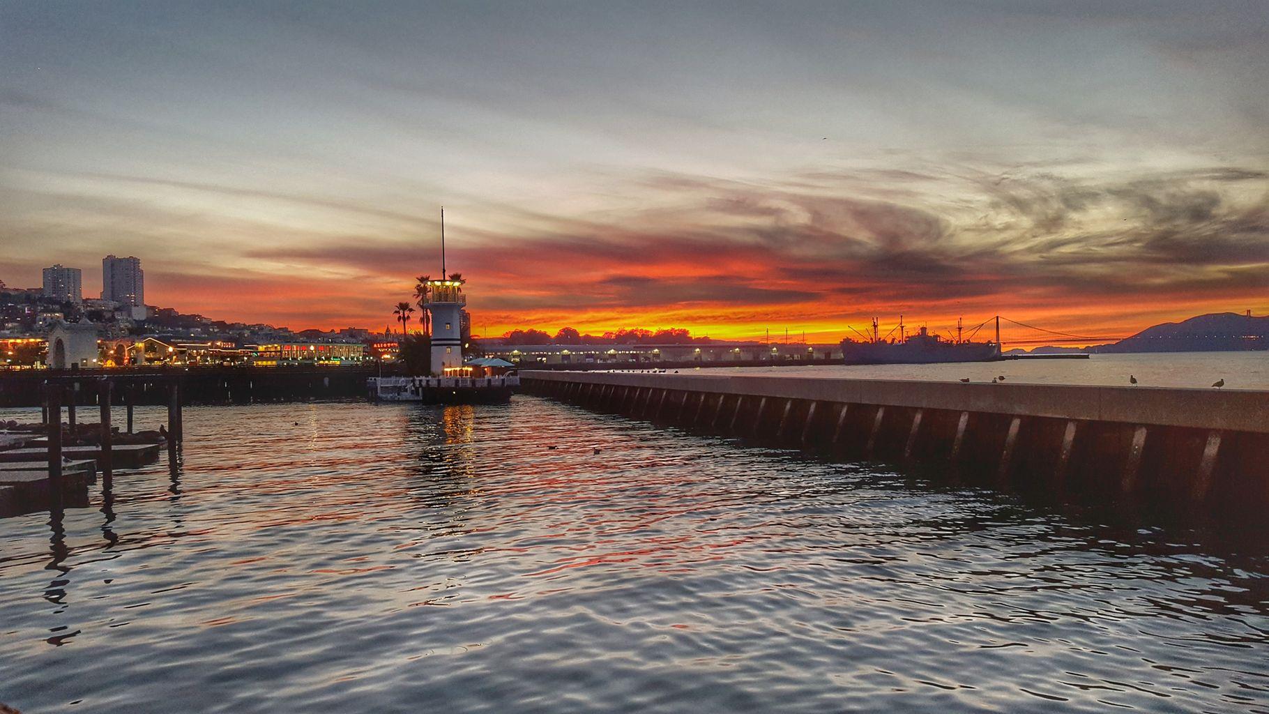 Pier with a lighthouse at sunset, vibrant orange and red sky.