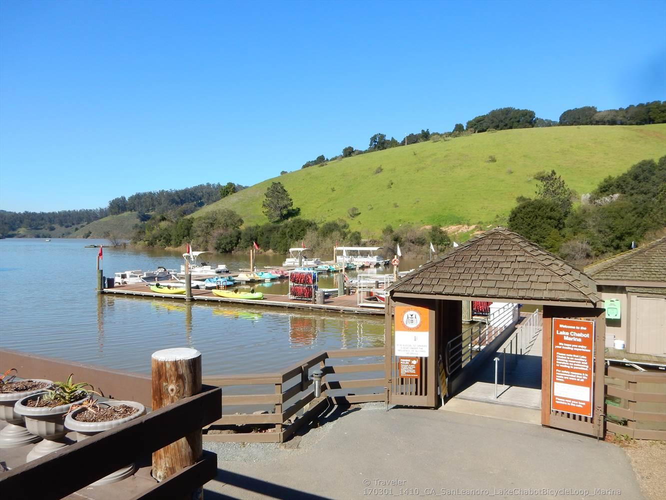 Sunny day at a boat dock on a lake with a green hillside.