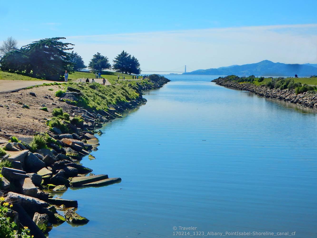 A sunny view of a calm canal leading to a distant bridge.