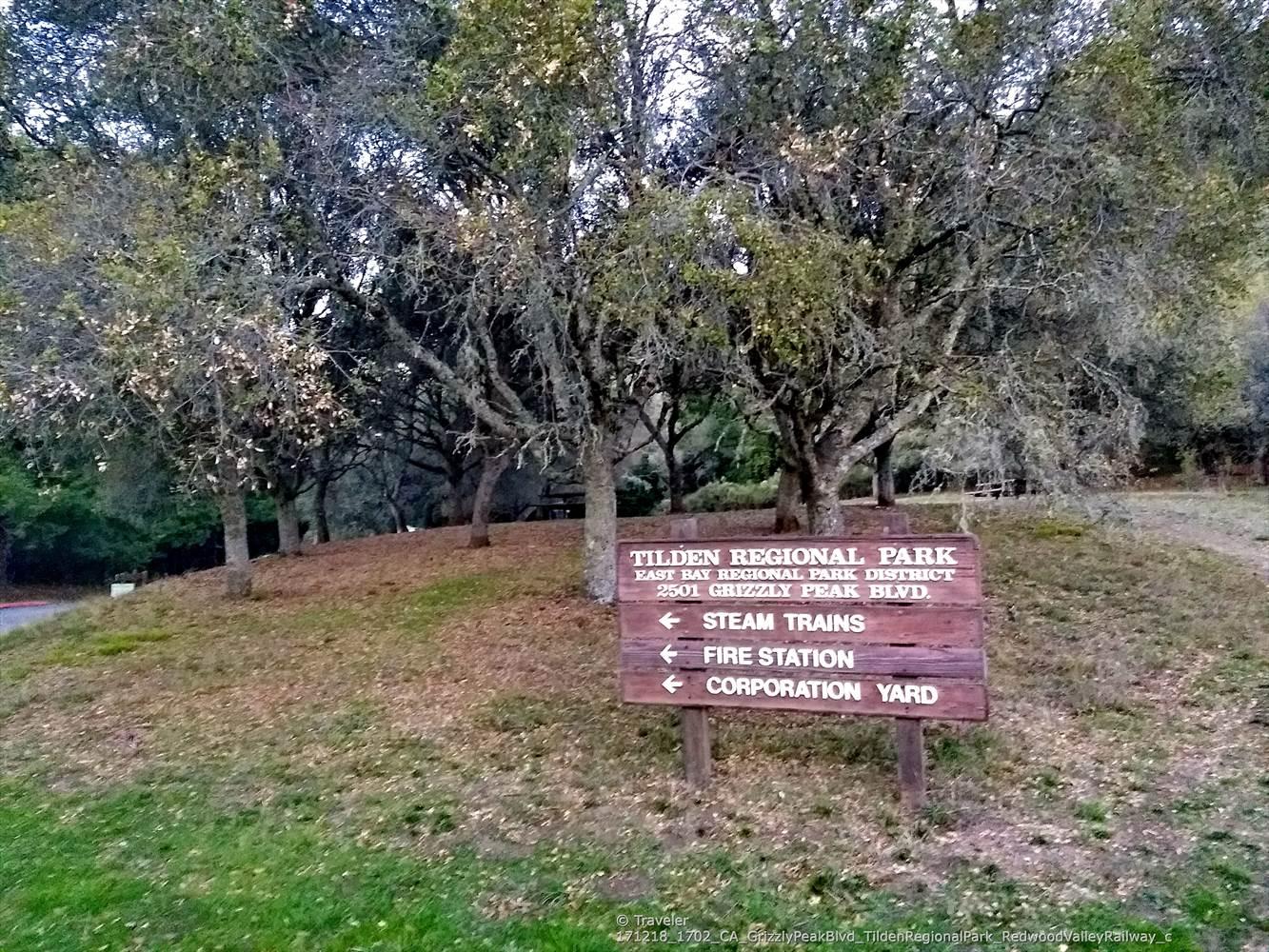 A wooden park sign on a grassy hill surrounded by trees.