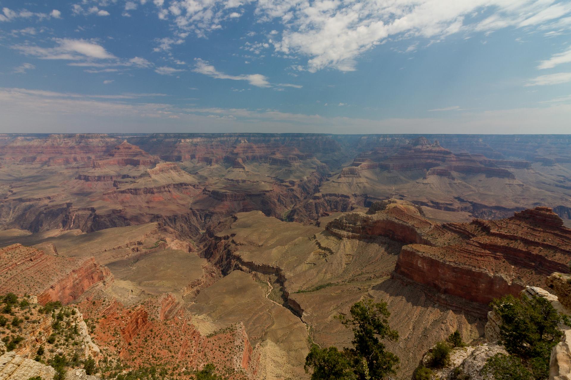 Vast canyon landscape with intricate rock layers under a blue sky.