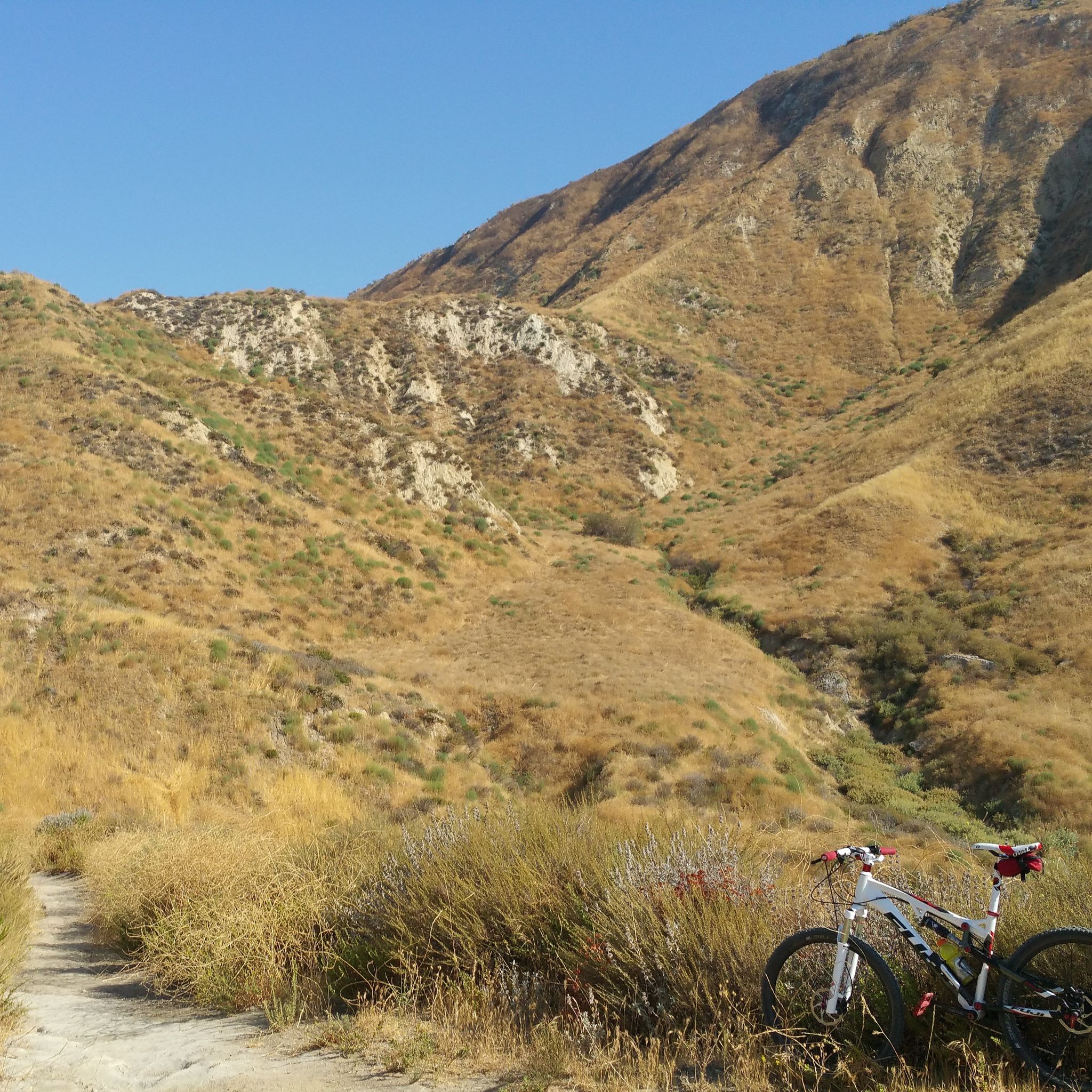 A mountain bike rests beside a dirt path on a steep, dry hillside. - Tapo Canyon Trail Loop