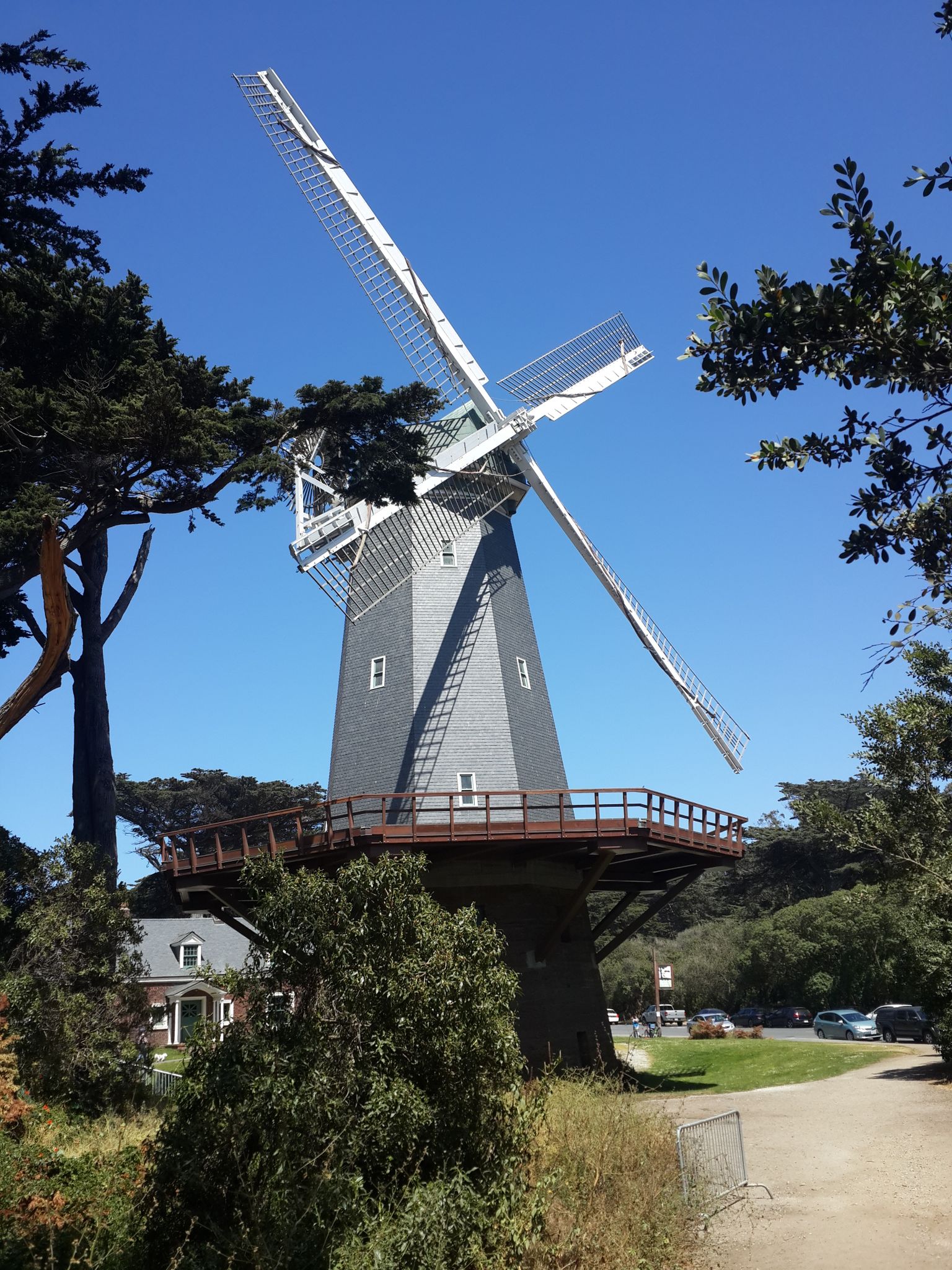 A tall grey windmill with white blades stands against a clear blue sky. - Murphy Windmill – Golden Gate Park loop from Judah Street & 9th Avenue