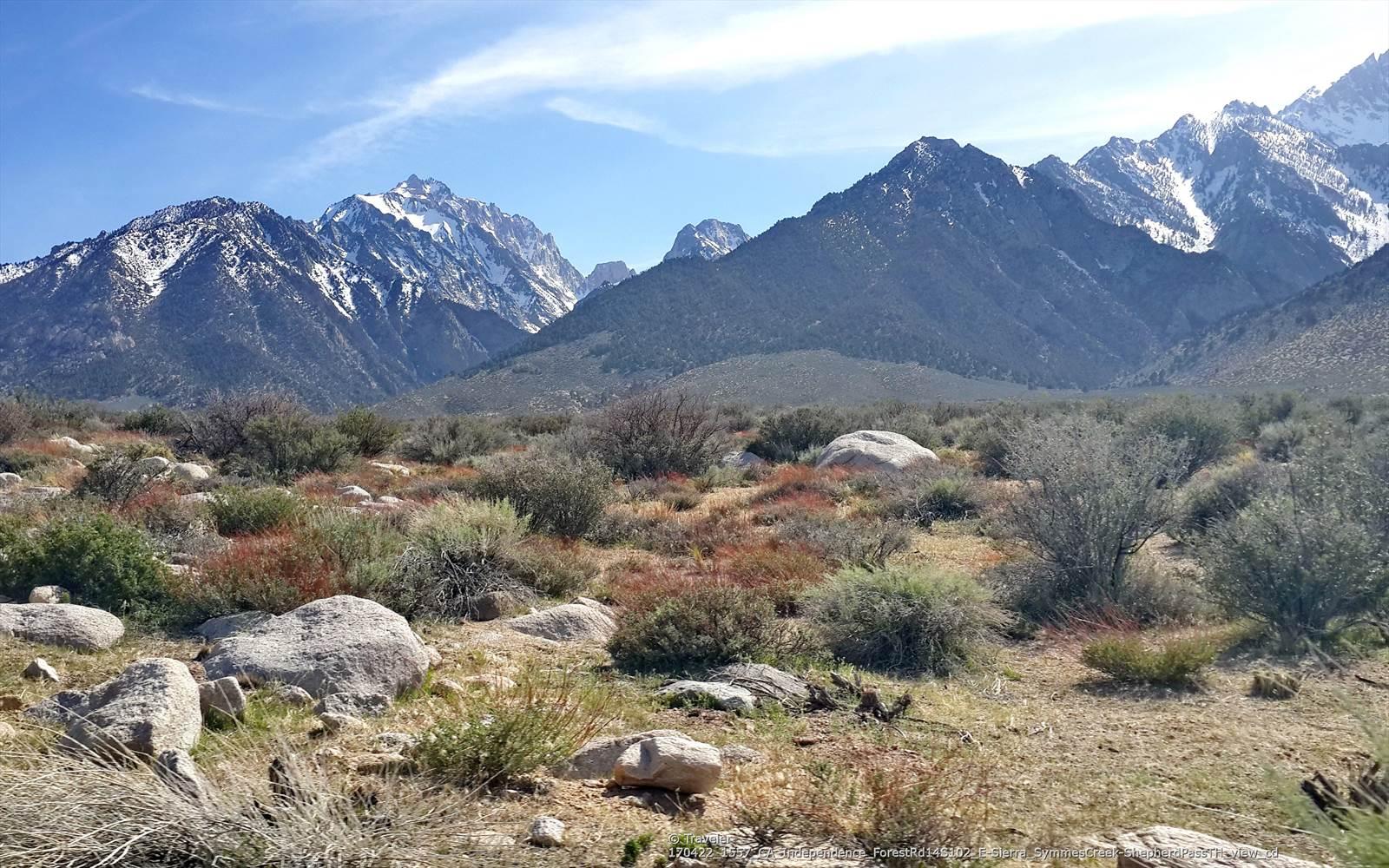 Snow-capped mountains rise above a landscape of dry brush and scattered rocks.