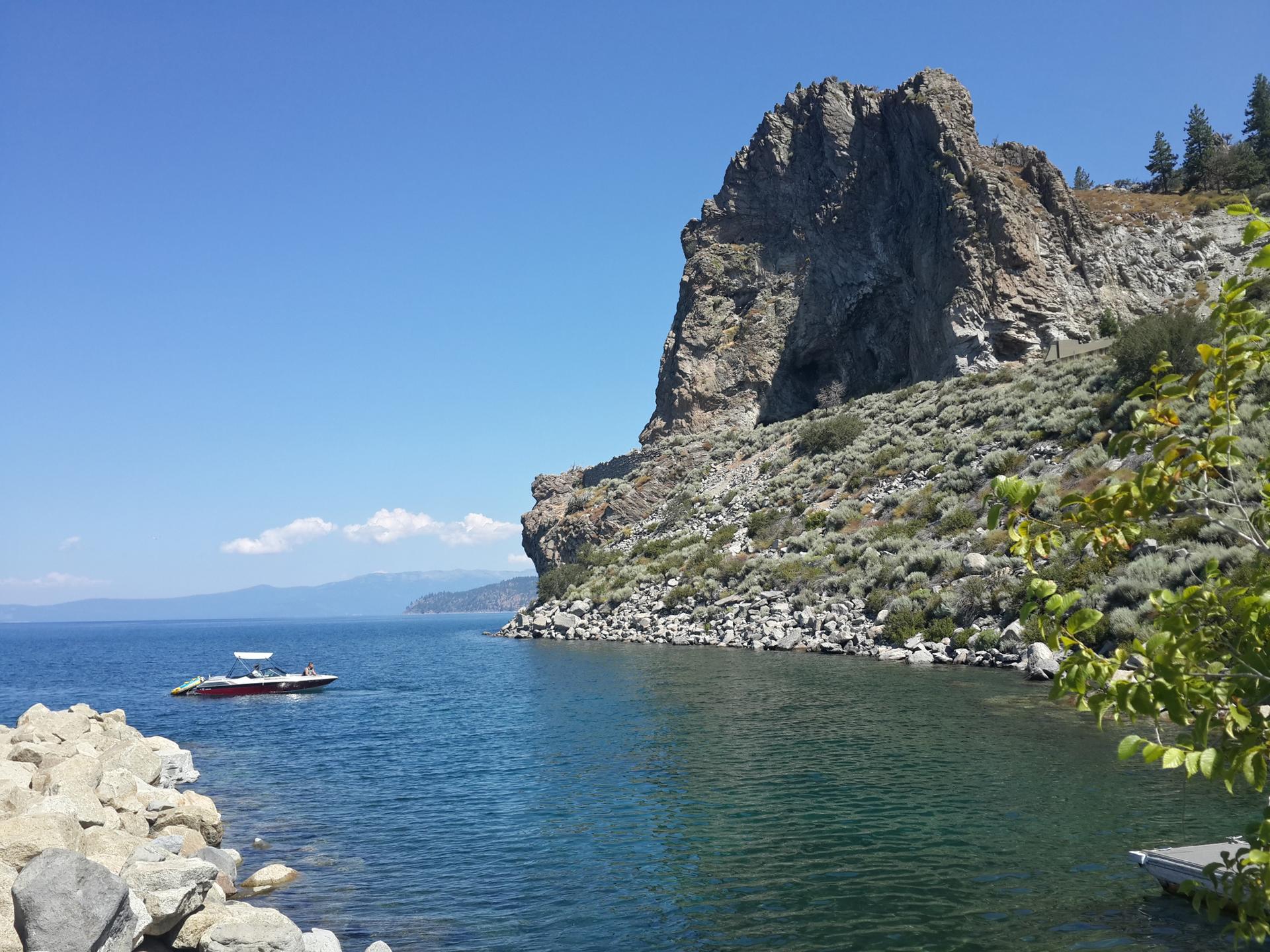 Steep rocky cliff overlooking a calm lake with a small boat.