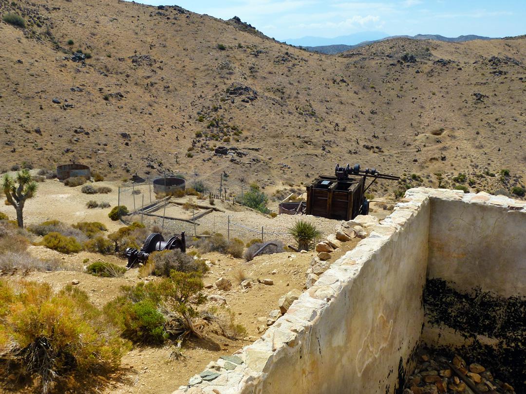Abandoned mining equipment and stone ruins in a dry, hilly desert landscape.