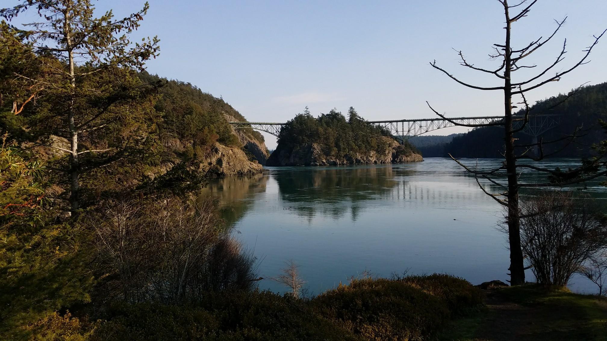 Golden hour light on a calm waterway with a distant bridge and forested shores.