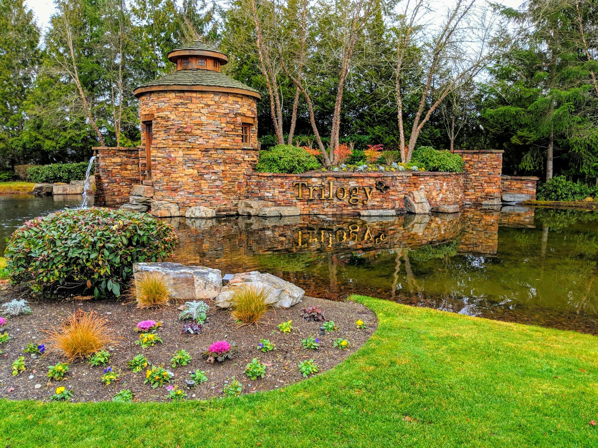 A stone tower and wall with a waterfall beside a pond, surrounded by lush landscaping.