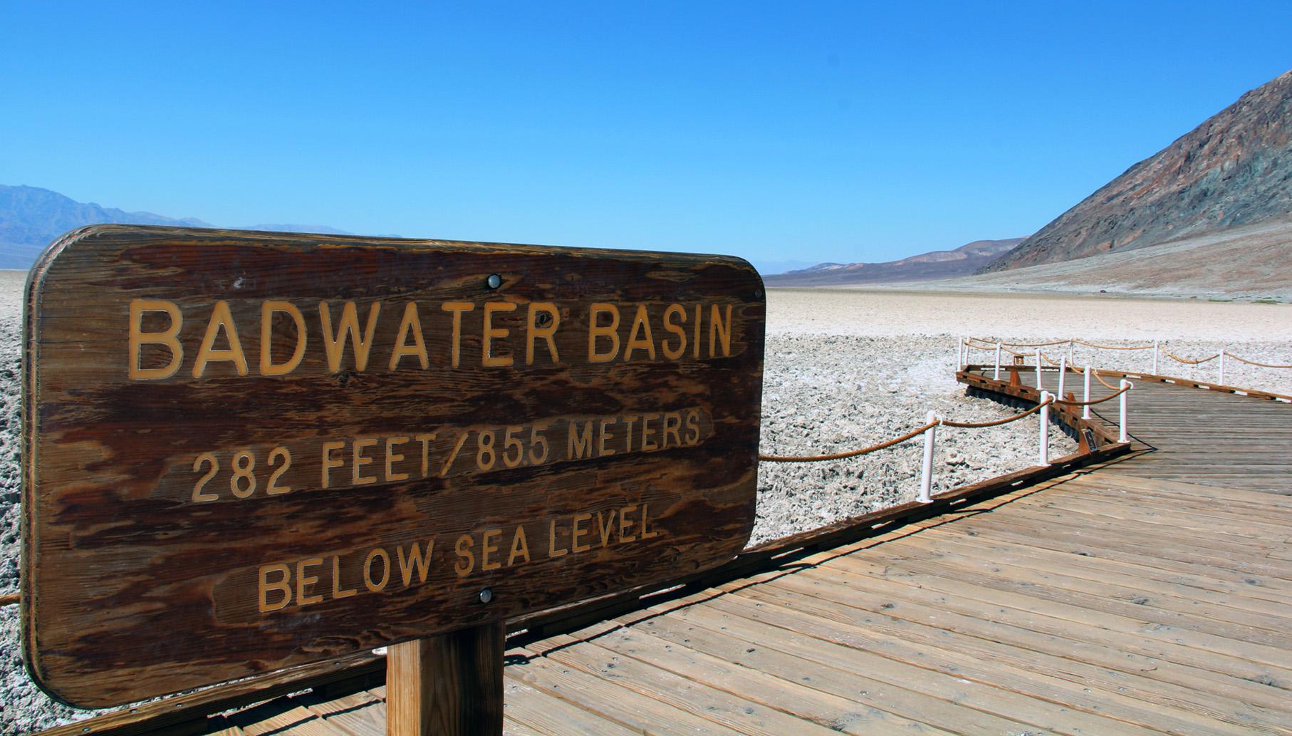 A wooden sign on a boardwalk overlooking a vast salt flat and mountains.