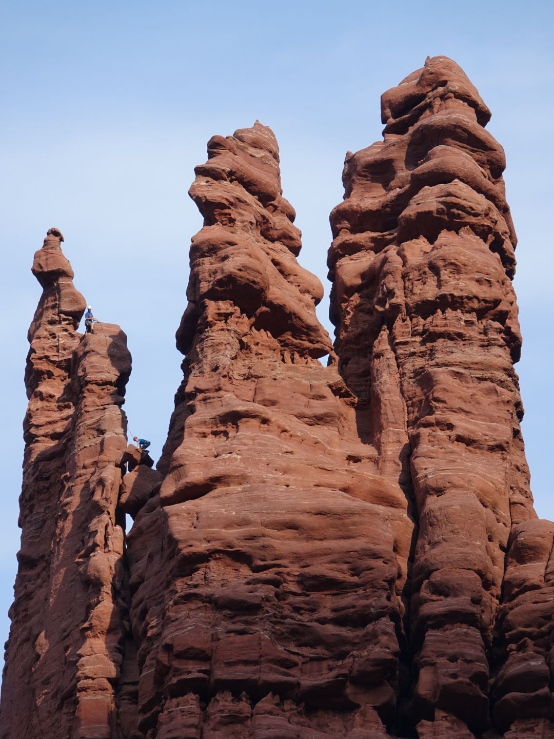 Close-up of three tall, weathered red rock spires against a light blue sky. - Fisher Towers Trail
