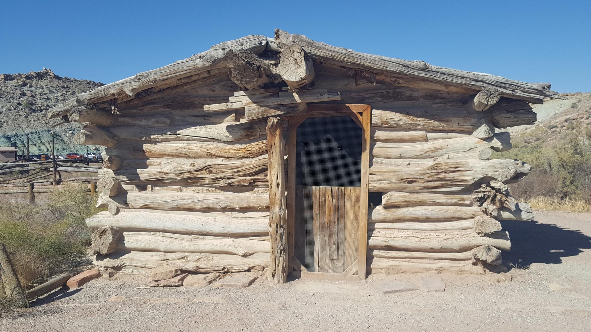 An old, rustic log cabin with a wooden door under a clear blue sky.