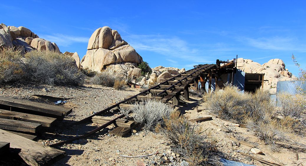 Old wooden mining ramp leading up a rocky desert hill under a clear blue sky. - Wall Street Mill Trail