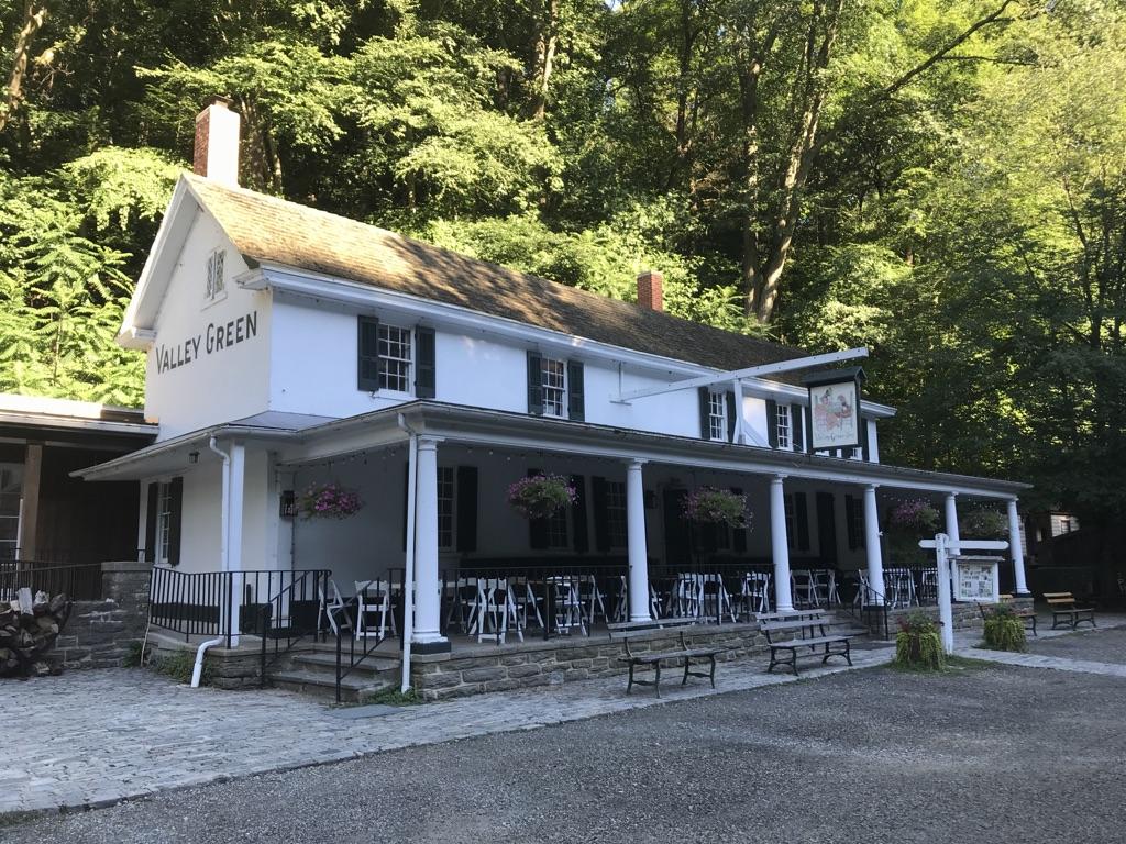 White building with large porch, "Valley Green" sign, sunny, outdoor seating.